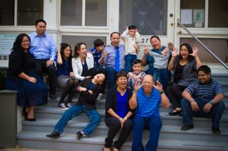 A large group, from children to older adults, making playful faces together on porch steps.