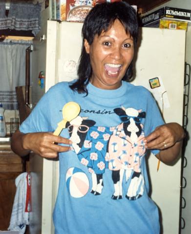 Marvel laughing while holding up a cow-print shirt in a kitchen.