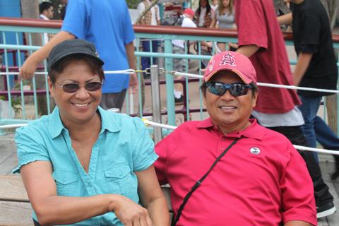 Marvel, on the left, sitting with another person outdoors, smiling, wearing sunglasses and caps.
