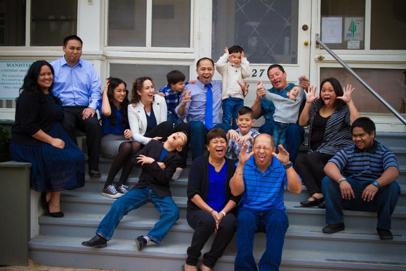 A large group, from children to older adults, making playful faces together on porch steps.